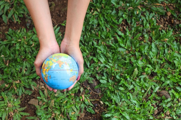 Фото Человеческие руки держат глобус мира на фоне природы зеленой травы. концепция дня земли.