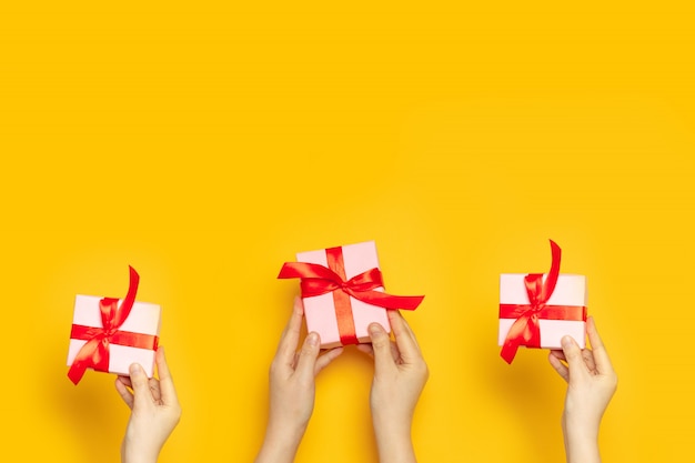 Human hands holds surprise boxes with red bow on a yellow background, top view