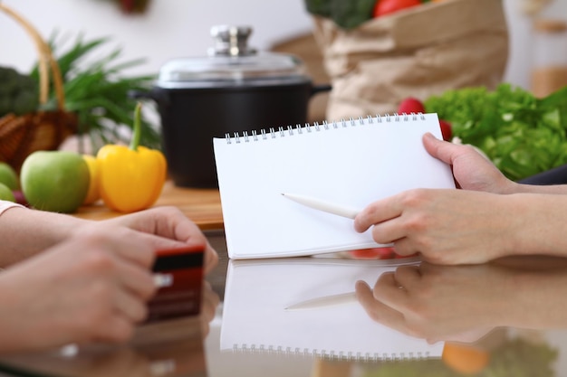 Human hands pointing into note book with copy space area. Two woman making menu in the kitchen, closeup. Cooking and friendship concept.