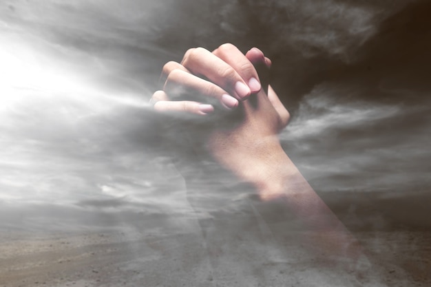 Human hands raised while praying to god with a dramatic sky background