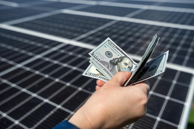 Human hands with a large amount of dollars in front of solar panels