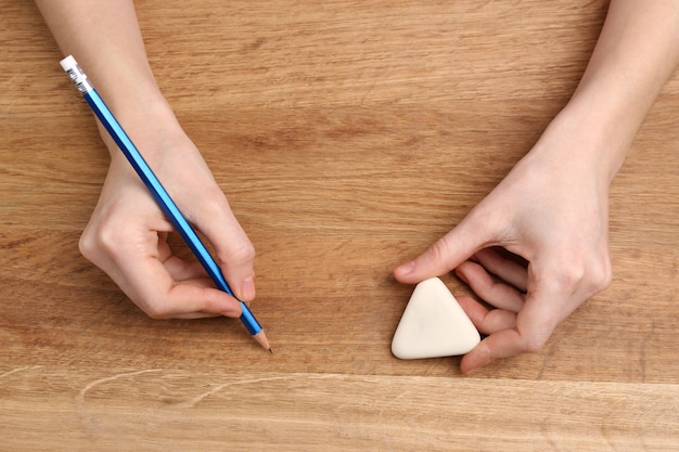 Human hands with pencil and erase rubber on wooden table