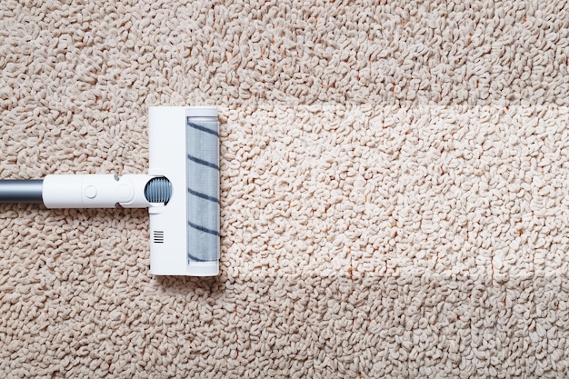 Фото Человеческие ноги и белая турбощетка беспроводного пылесоса чистят ковер в доме. современные технологии очистки.