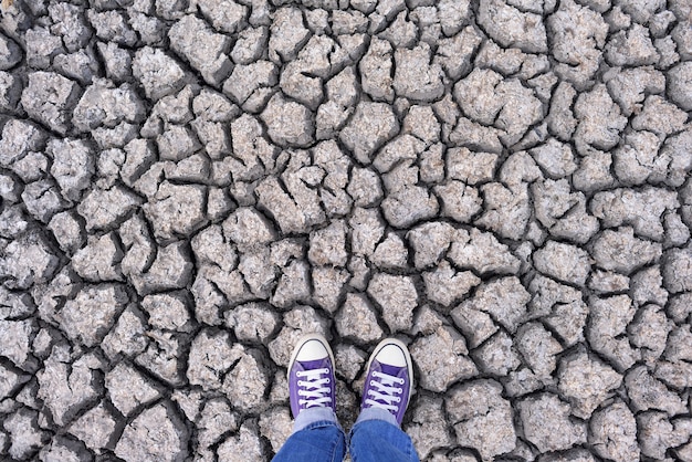 Human legs in sneakers and jeans standing on dried cracked earth, background