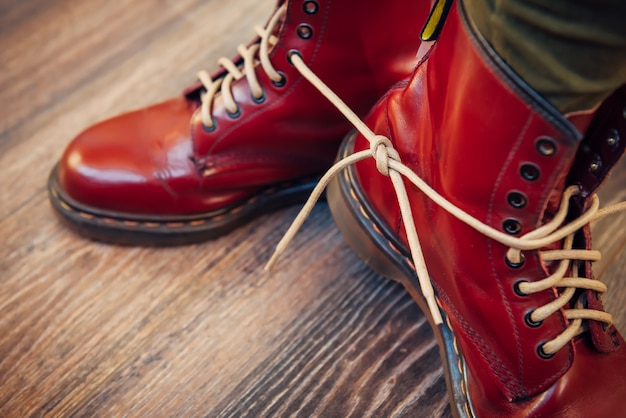 Human legs in stylish bright red boots with thick white laces tied together on wooden