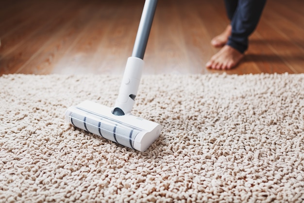 Human legs and a white turbo brush of a cordless vacuum cleaner cleans the carpet in the house. Modern technologies for cleaning.