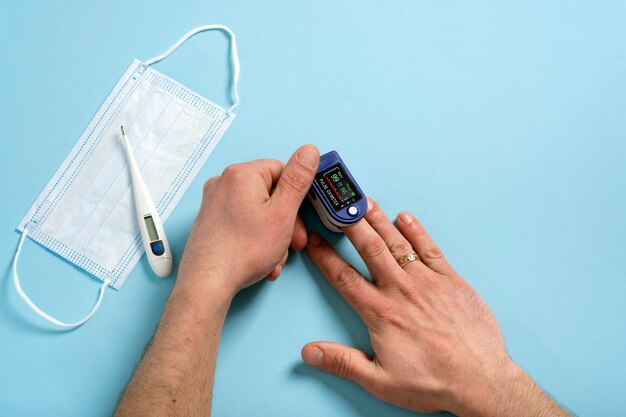 人間の男性の手のパルスオキシメータは、コピースペースのある医療用の青い背景で脈拍数と酸素レベルを測定するために使用されます。