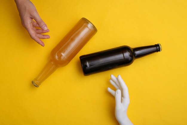 Human and mannequin hand touching beer bottle on yellow background