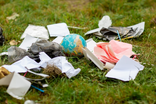 Человеческая халатность Глобус в кучу разбросанного мусора на фоне зеленой травы.