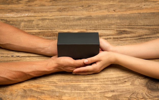 Human's hand holding a present, gift, surprise box isolated on wooden background. Concept of celebration, holidays, family, home comfort, winter's holidays, New Year eve, birthday, anniversary