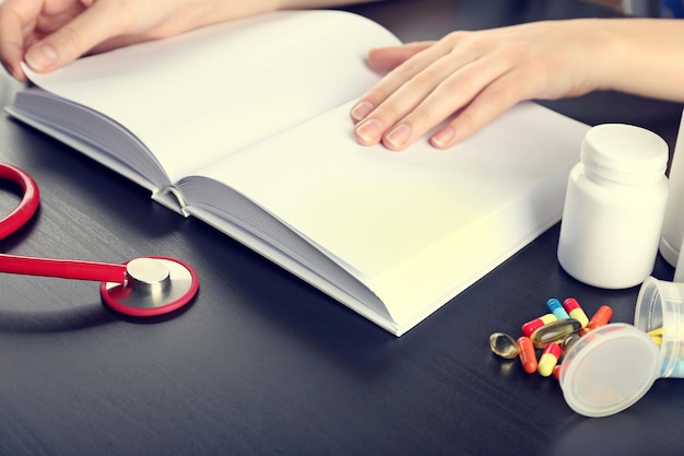 Foto le mani dell'essere umano sul libro medico con le pillole e il primo piano rosso dello stetoscopio