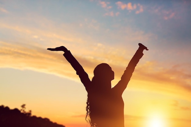 Human silhouette with raising hands on the sunset background