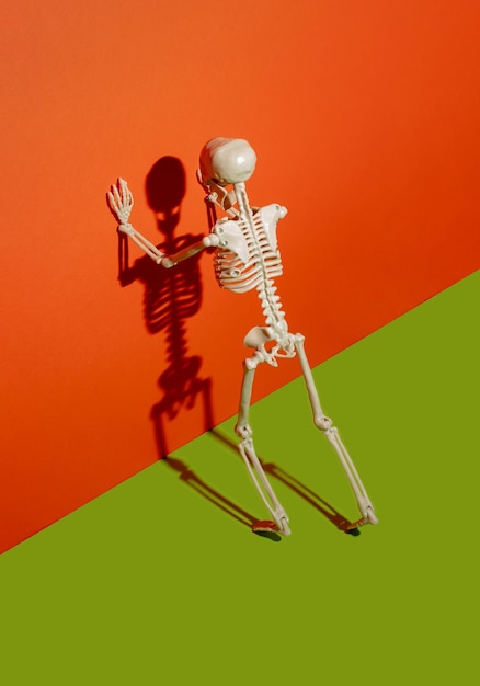 Human a skeleton pushes the orange wall orange wall and a shadow skeleton Creative Halloween concept Minimal horror wallpaper 31th October party invitation card with copy space