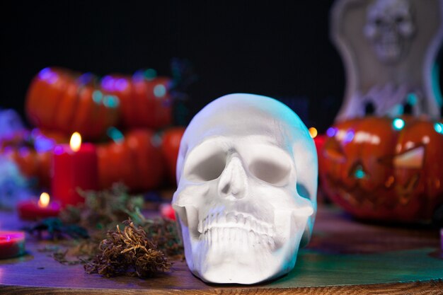 Human skull sitting on a wooden table with scary pumpkin celebrating halloween. Halloween candles.