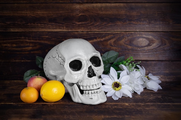 Human skull with flowers and fruits on wooden surface