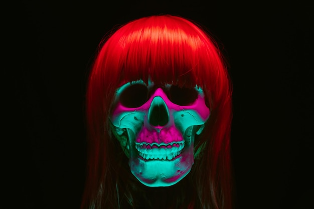 Photo human skull of a woman in a wig with red hair with colored pink green light