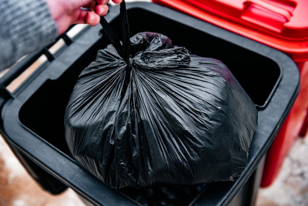 Human throwing garbage in black trash cans.