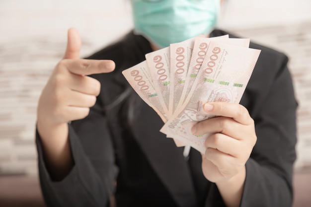 Photo a human wearing a medical mask and a black suit pointing the money in her hand.