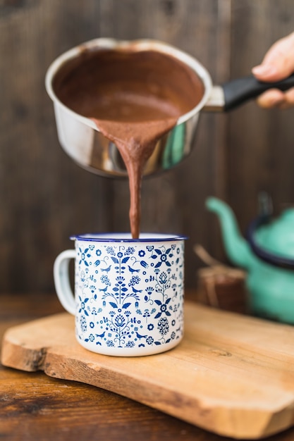 Human with sauce pan pouring brown liquid in cup