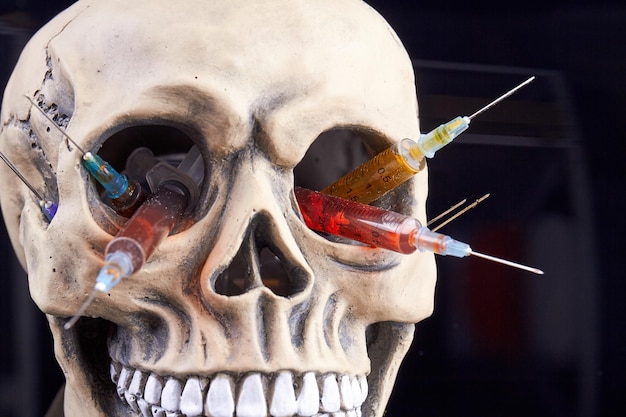 Humans skull with syringes filled with colorful liquid danger of drugs concept isolated on black bac