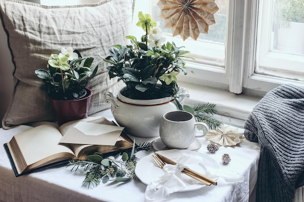 Humeurig winterontbijt stilleven scène Kerst feestelijke tafel setting met gouden bestek kopje koffie wenskaart eucalyptus en dennenboom takken Ingemaakte hellebores bloemen bij het raam