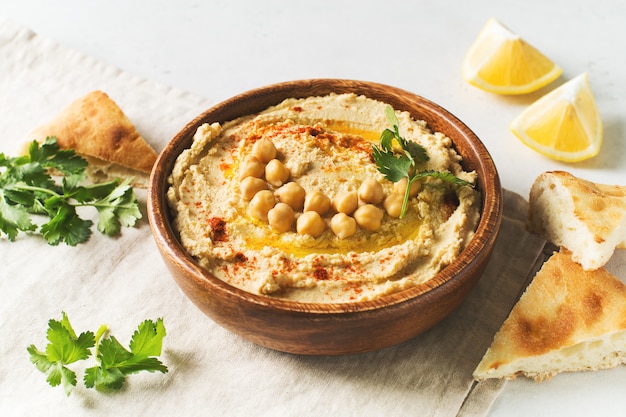Photo hummus dip with chickpea, pita  and parsley in wooden plate on white background
