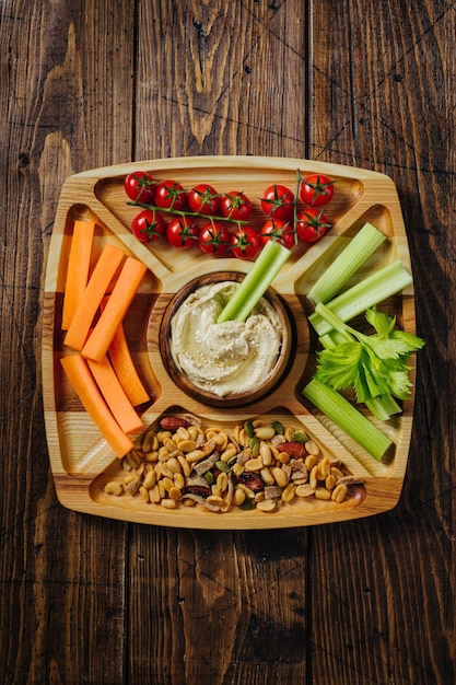 Foto hummus en groentesticks van wortel en bleekselderij op een houten bord