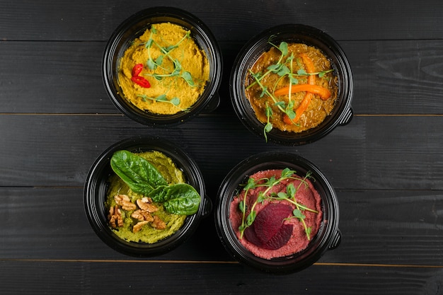 Hummus garnished peppers, chili, beet and herbs in black bowl on dark wooden table