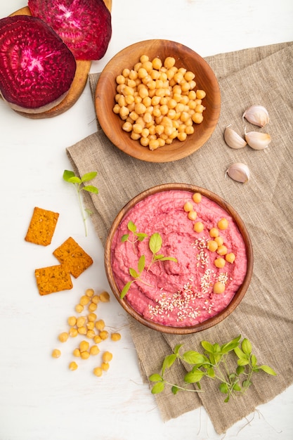 Hummus met bieten en microgroene basilicumspruiten in houten kom op een witte houten lijst.