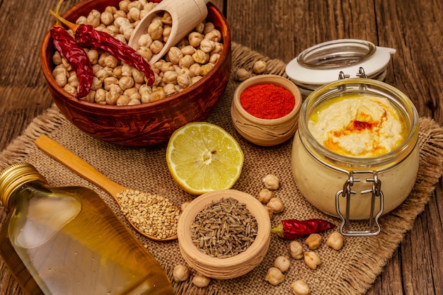 Hummus on old wooden table. Dry chickpea, olive oil, lemon, cumin and chili pepper