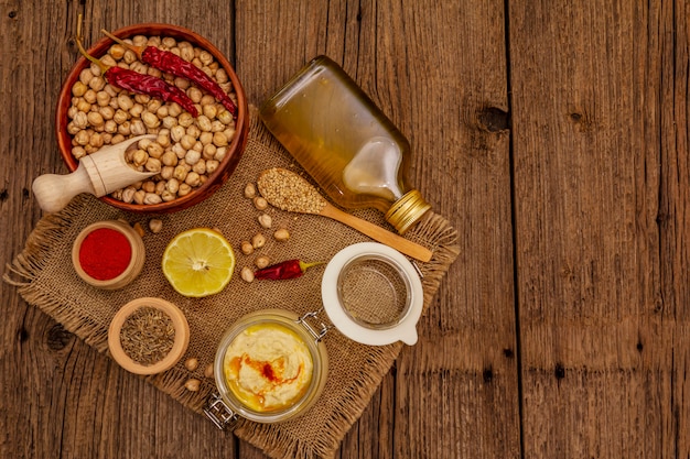 Hummus on old wooden table. Dry chickpea, olive oil, lemon, cumin and chili pepper