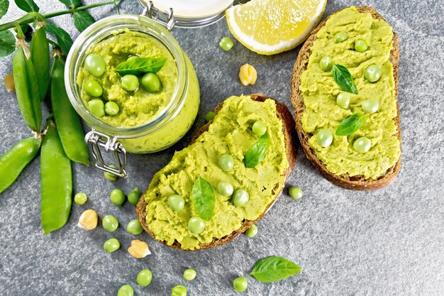 Hummus sandwiches with green peas and chickpeas jar of dipping\
sauce pea pods on granite countertop background from above