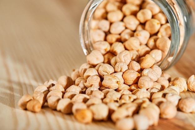 Hummus seeds spilled out of a glass jar on a wooden surface