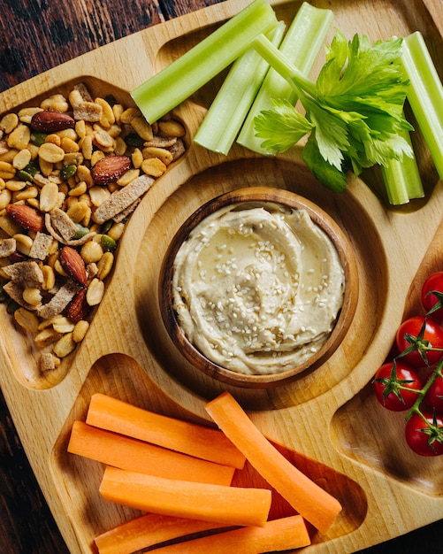 Hummus and vegetable sticks of carrot and celery on a wooden plate