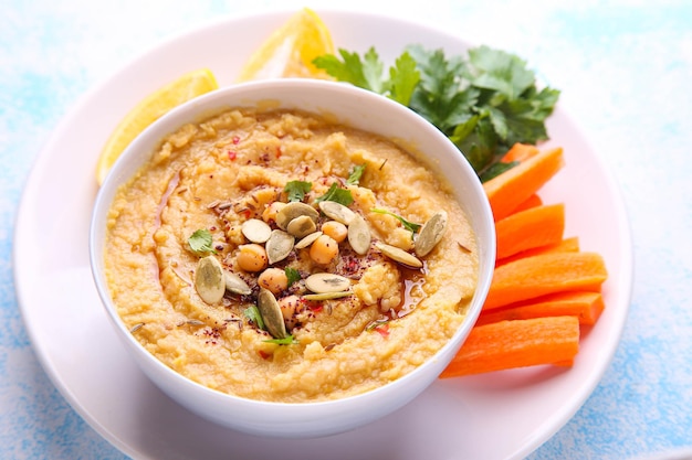 Hummus in a white plate with carrots, lemon and spices