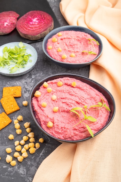 Hummus with beet and microgreen basil sprouts in ceramic bowl on a black concrete surface and orange textile