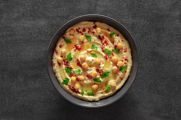 Hummus with chickpeas oil and spices in grey bowl on dark background top view on center