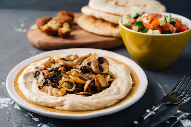 Hummus with fried mushrooms, cucumber and tomato salad, falafel and pita