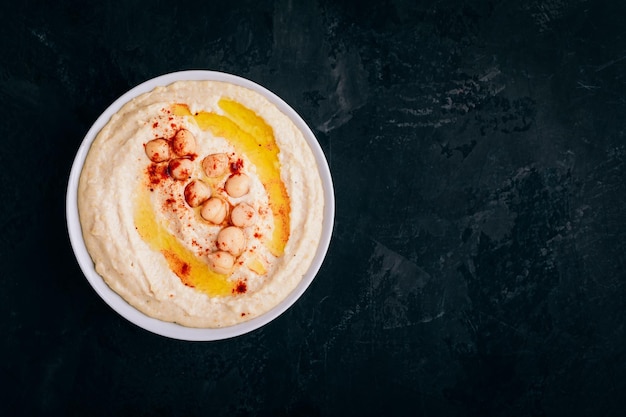 Hummus with olive oil and chickpea in bowl on dark stone background Top view with copy space