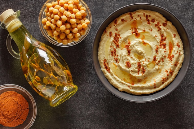 Hummus with olive oil and red pepper in grey bowl on slate stone plate round dark background top view