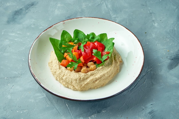 Hummus with vegetables and spinach in a white bowl