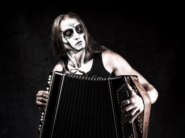 Humorous portrait of man in goth style clothes and scull makeup with the bayan button accordion