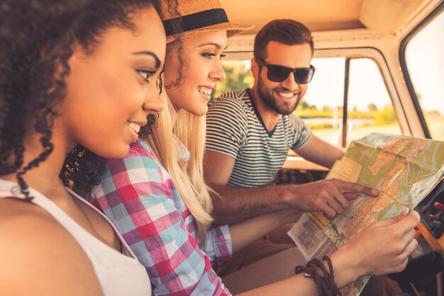 Hun roadtrip plannen. Zijaanzicht van drie vrolijke jonge mensen die kaart onderzoeken en glimlachen terwijl ze in hun minibusje zitten