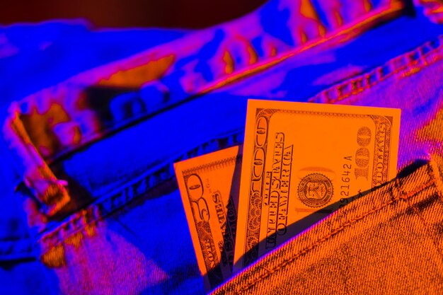 Hundred dollar bill in pocket of blue jeans toned Dollars in neon light Banknotes