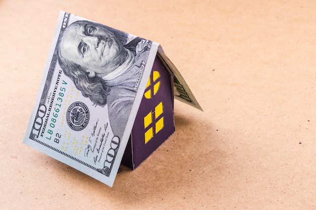 Крыша стодолларовой банкноты покрывает фиолетовый картонный дом.