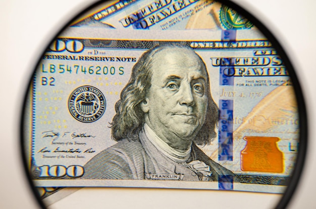 Стодолларовые банкноты США под увеличительным стеклом.