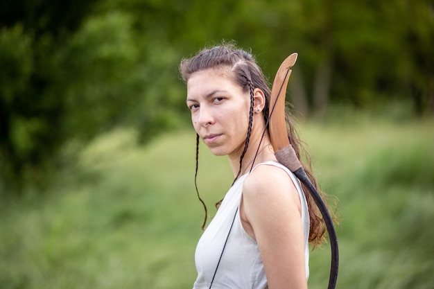 A Hungarian woman in a linen dress standing with a bow on the field