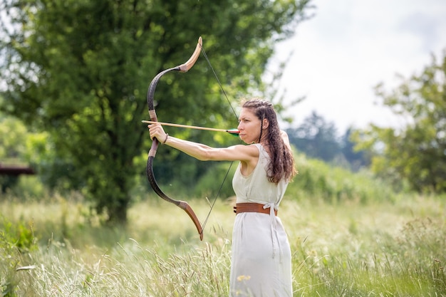 Photo a hungarian woman in a linen dress standing with a bow in the tall grass