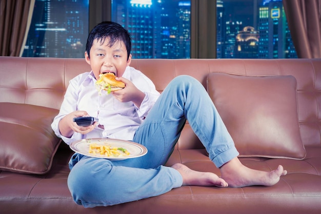ソファに座りながらハンバーガーを楽しむ空腹の少年
