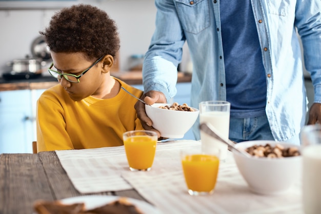 Non affamato. simpatico ragazzo pre-adolescente che distoglie la faccia da suo padre che gli dà una ciotola di cereali, esprimendo la sua riluttanza a mangiare